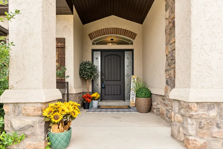 Textured stucco exterior with stone accents, arched entryway, dark wood-finish door with decorative glass sidelights, and recessed overhead lighting