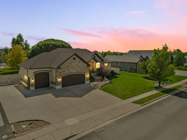 Stucco and stone exterior with a multi-car driveway, attached two-car garage, and established landscaping
