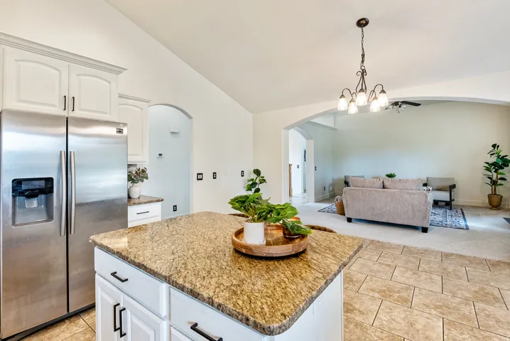 Kitchen island with a granite-style countertop, white cabinetry with dark hardware, and ceramic tile flooring
