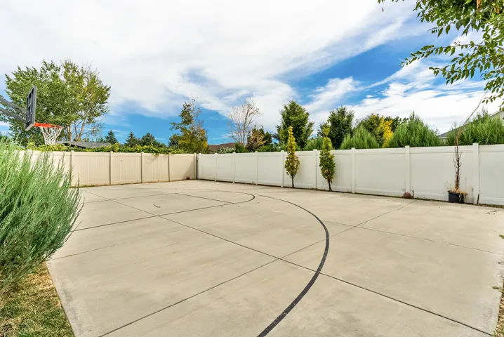 Expansive concrete patio with painted court lines and a basketball hoop, surrounded by a tall white privacy fence