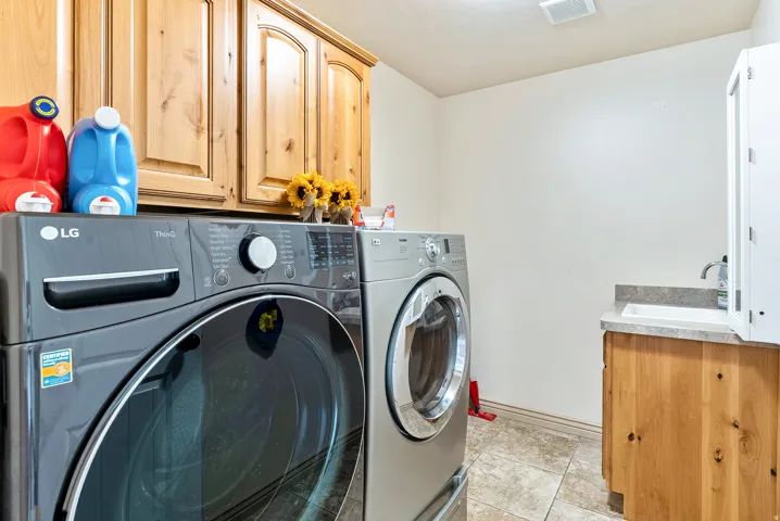 Laundry area featuring tile flooring, wood-finish cabinetry, a single basin sink, and a countertop