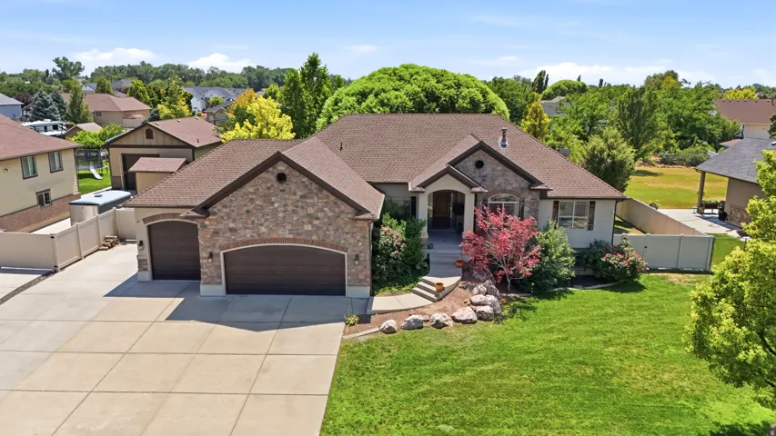 Stone and stucco exterior residence featuring a substantial front lawn, mature landscaping, a two-car garage, and a concrete driveway