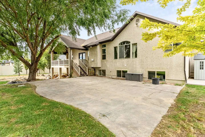 Stucco exterior with multiple window styles, concrete patio, covered deck with white railing, exterior staircase, and mature trees