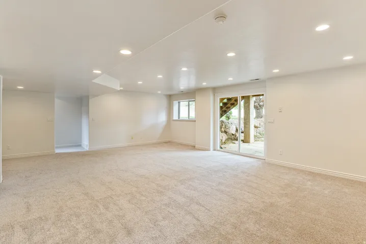 Expansive carpeted room with recessed lighting, white walls, a visible window, and a sliding glass door