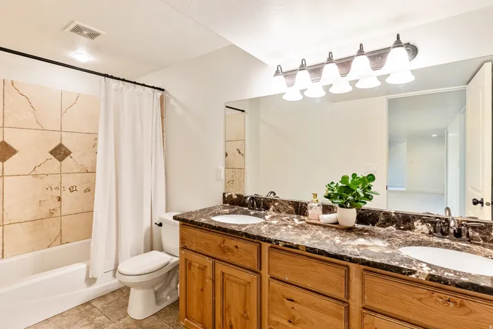 Dual vanity with a stone countertop, light wood-finish cabinetry, and undermount sinks