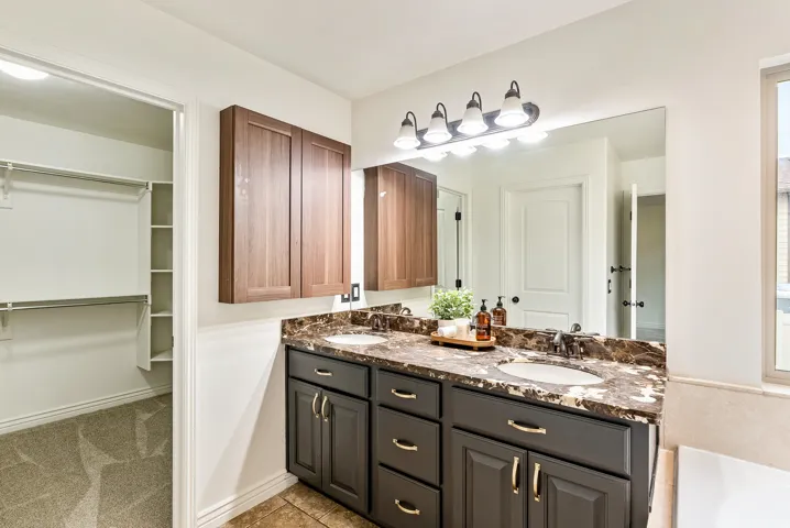 Dual vanity with dark cabinetry, stone countertop, and integrated sinks