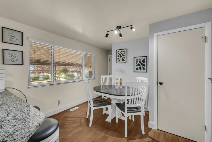 Wood-finish flooring, track lighting, a large window with blinds, and a built-in granite-finish counter