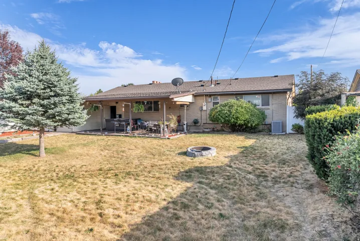 Expansive backyard featuring a covered patio, stone fire pit, mature trees, and a privacy fence