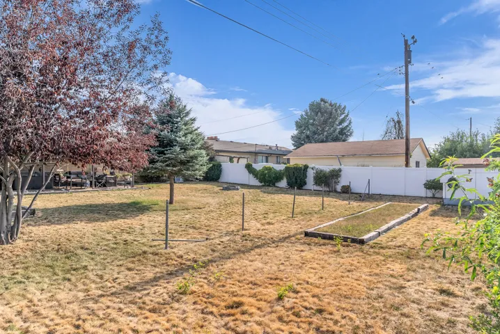 Expansive backyard featuring a white privacy fence, mature trees, and a built-in garden bed