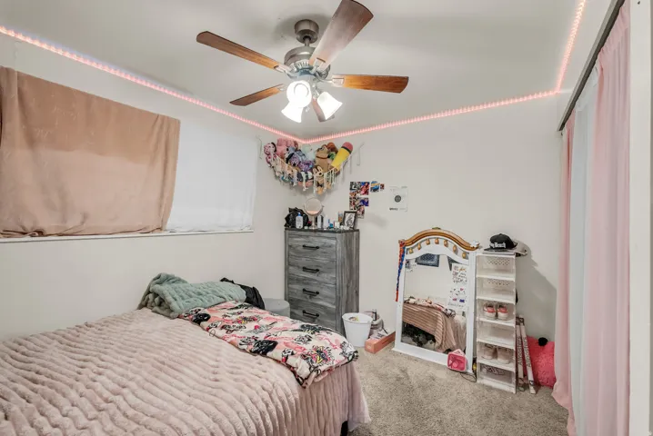 Ceiling fan with wood-finish blades, white walls, and wall-to-wall carpeting