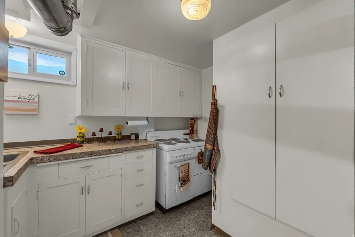 White cabinetry with brushed nickel hardware, stone-finish countertops, built-in sink, and compact electric range