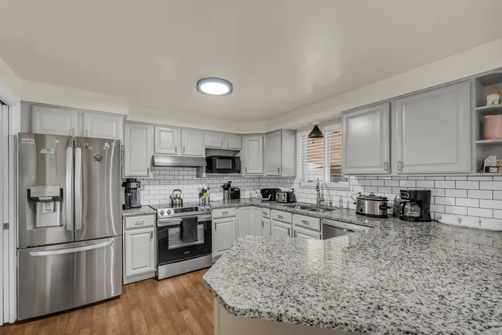 Kitchen featuring wood-finish flooring, stainless steel appliances, light gray cabinetry, white subway tile backsplash, and speckled countertops