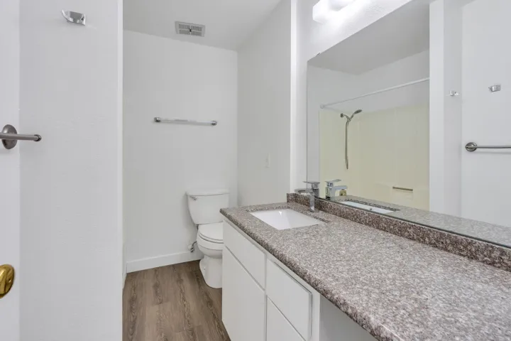 Bathroom featuring a vanity with an integrated sink, a large mirror, a speckled countertop, white cabinetry, and wood-finish flooring