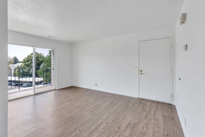 Wood-finish flooring, white painted walls, sliding glass door, and a private balcony with black metal railing