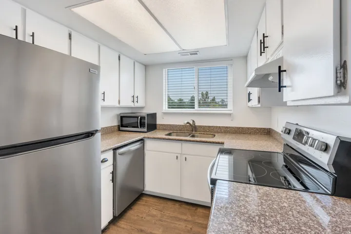 Kitchen featuring stainless steel appliances, white cabinetry with dark hardware, a double basin sink, and wood-finish flooring