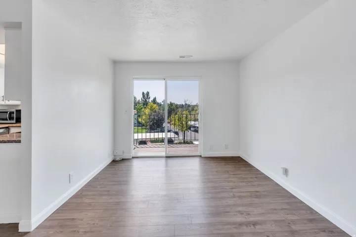 Wood-finish flooring with white baseboards, bright white walls, and a sliding glass door leading to a balcony with black metal railings