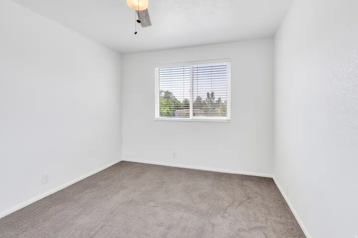 Neutral-toned carpeting, white walls, window with blinds, and a ceiling light fixture