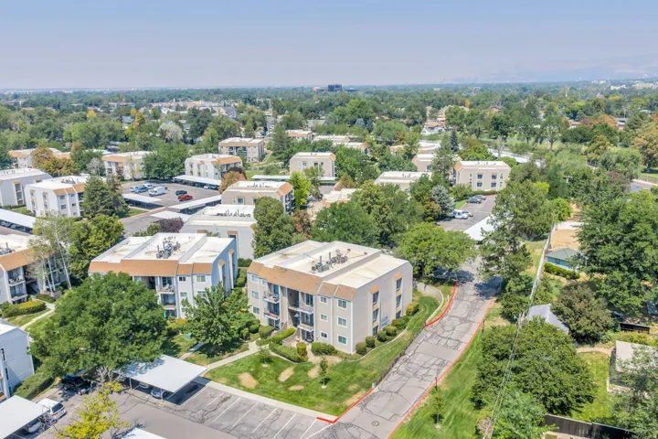Community setting with multiple residential buildings, abundant mature trees, and designated covered parking areas