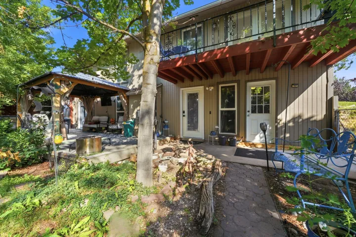 Lower-level patio with direct outdoor access, covered gazebo, upper balcony with iron railing, and a stone-paver pathway
