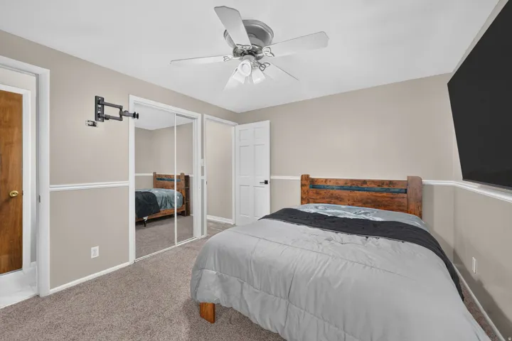 Neutral wall paint with chair rail molding, ceiling fan, and mirrored closet doors