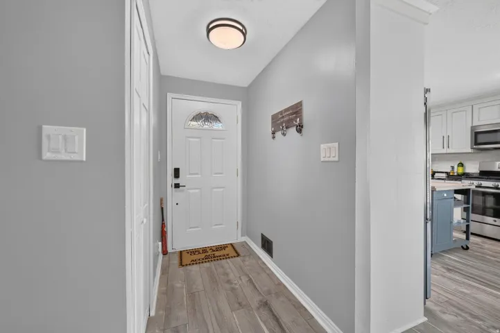White paneled entry door with decorative glass insert, dark hardware, and wood-finish flooring