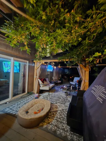 Spacious outdoor patio area featuring a sliding glass door, a covered pergola, and string lighting
