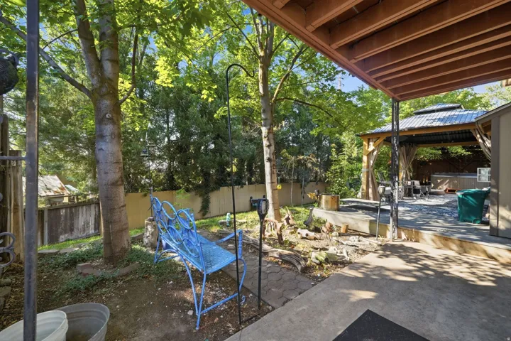 Covered patio area, mature trees, concrete hardscaping, wood deck structure, and a gazebo