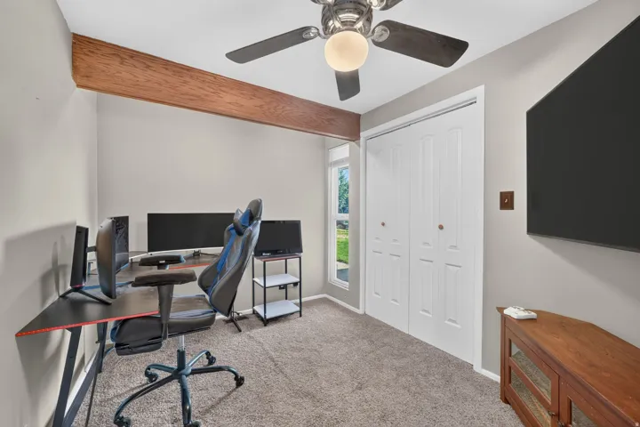 Recessed window with white trim, built-in bi-fold closet doors, ceiling fan with light fixture, and exposed wood beam