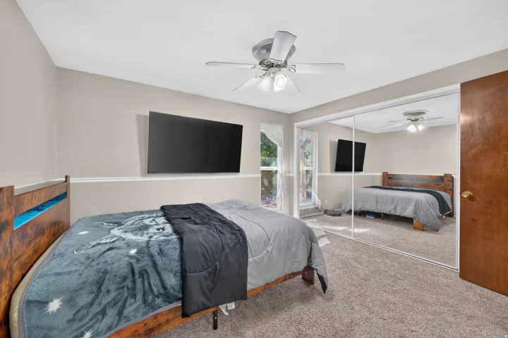 Ceiling fan, wall-mounted television, neutral wall paint, mirrored closet doors, and wood-finish door