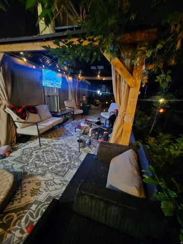 Covered outdoor patio with a corrugated metal roof, string lighting, and privacy curtains