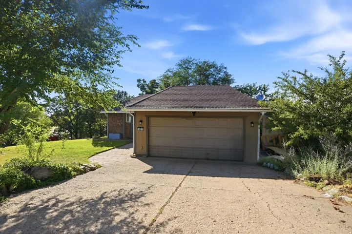 Attached two-car garage with a concrete driveway, complemented by mature trees and established landscaping