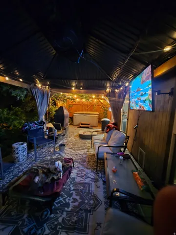 Covered outdoor area featuring a hot tub, string lighting, and privacy drapes