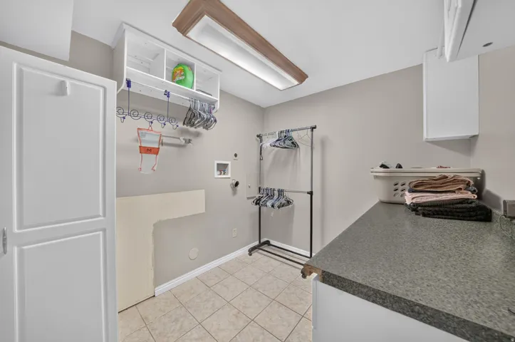 Integrated laundry room featuring tile flooring, counter space, built-in cabinetry, and overhead lighting