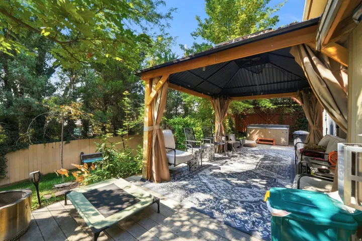 Paved patio with an integrated gazebo featuring curtains, a built-in hot tub, and a privacy fence