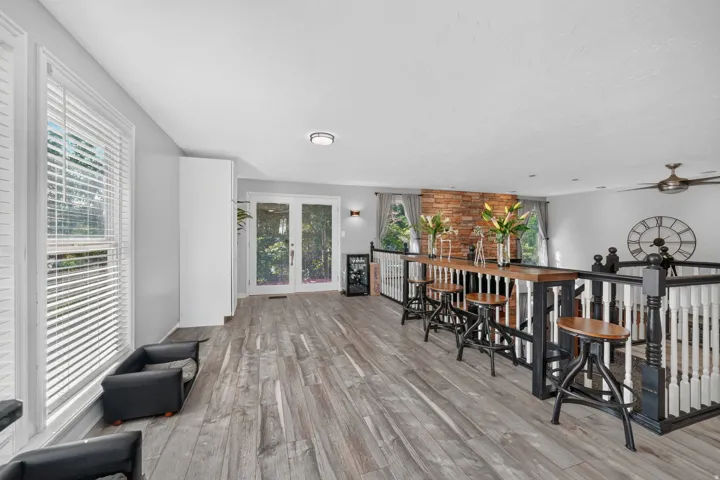 Wood-finish flooring, white double French doors, built-in bar, and white and black banister