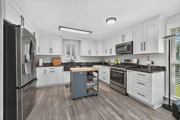 White shaker-style cabinetry with matte black hardware, stainless steel appliances, dark stone countertops, wood-finish flooring, and subway tile backsplash