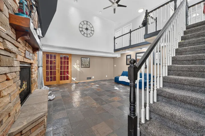 Stone-clad fireplace with mantel, French doors, slate tile flooring, carpeted staircase, and an upper-level balcony