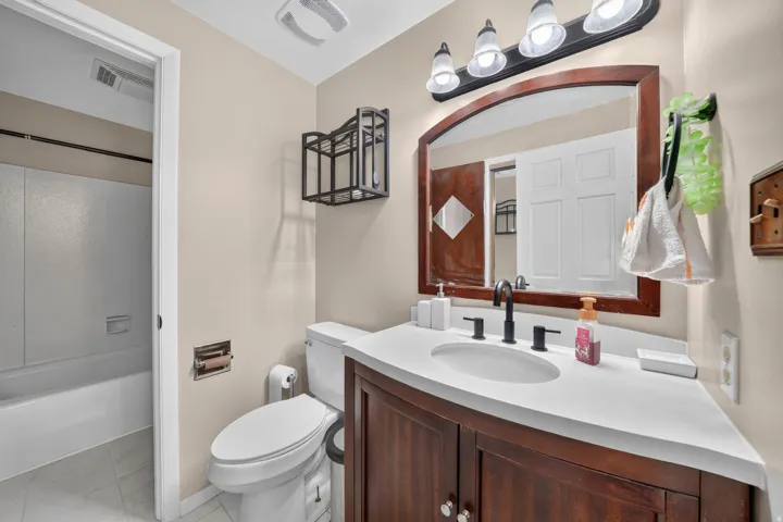Wood-finish vanity with an integrated sink and matte black faucet, framed mirror, and a full-size bathtub with tile surround
