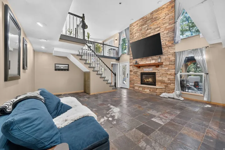 Stone-clad fireplace with wood mantel, high ceilings, multi-level staircase with white spindles, and slate tile flooring