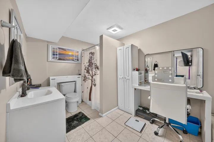 White vanity with integrated sink, toilet, tiled flooring, and a white storage cabinet