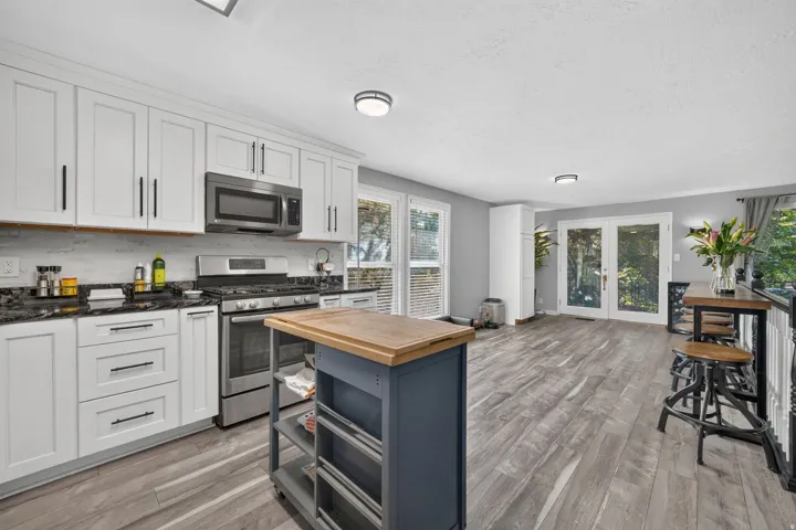 Contemporary kitchen featuring white cabinetry, stainless steel appliances, dark stone countertops, and wood-finish flooring
