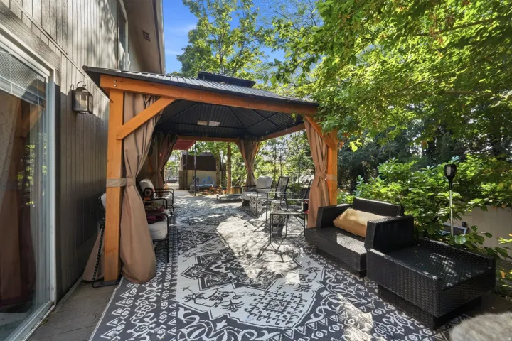 Patio with a pergola, exterior wall light fixture, and surrounding greenery