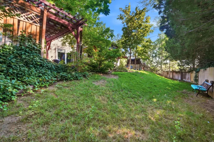 Terraced backyard with a wooden pergola, mature trees, and privacy fencing