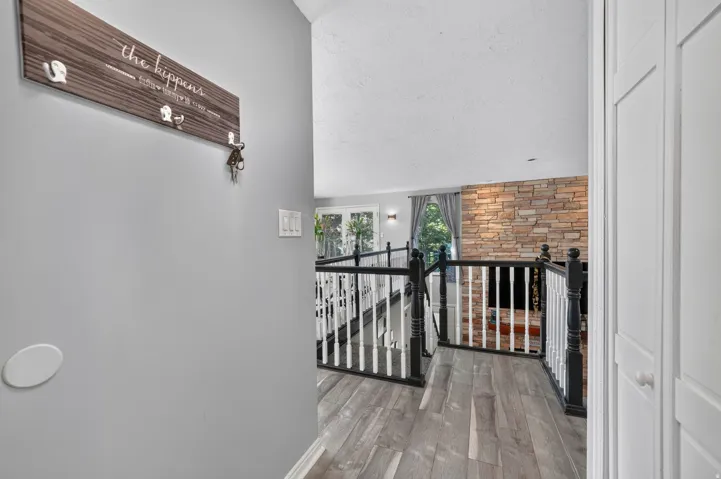 Stone-clad fireplace with a hearth, wood-finish flooring, and white spindle railing with dark wood newel posts