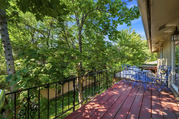 Expansive wood-plank balcony with a black wrought-iron railing, surrounded by mature trees