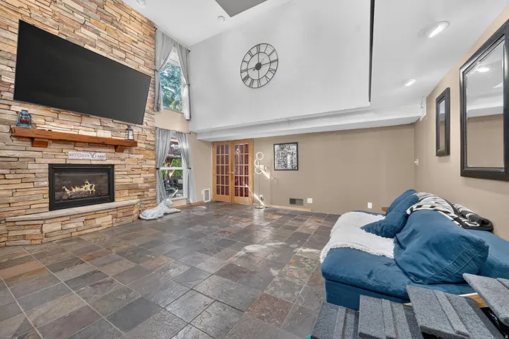 Stone-clad fireplace with wood mantel, tile flooring, high ceilings, recessed lighting, and French doors