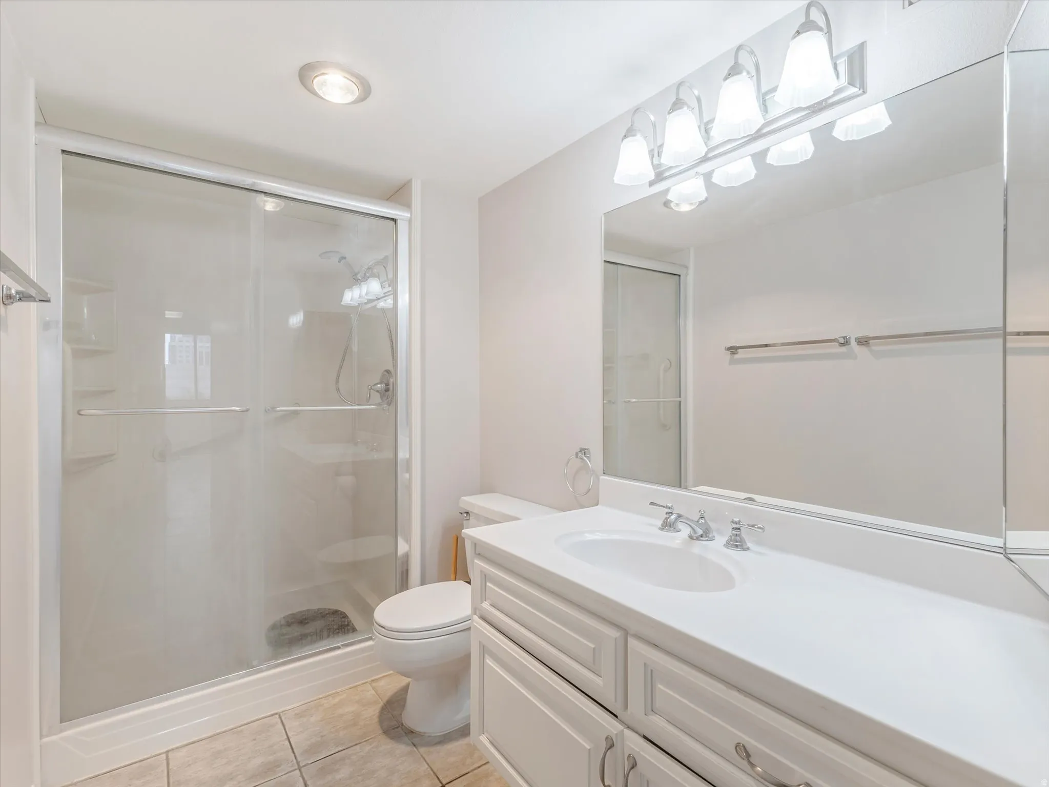 Recessed lighting, tile flooring, glass-enclosed shower, vanity with integrated sink, and wall-mounted mirror