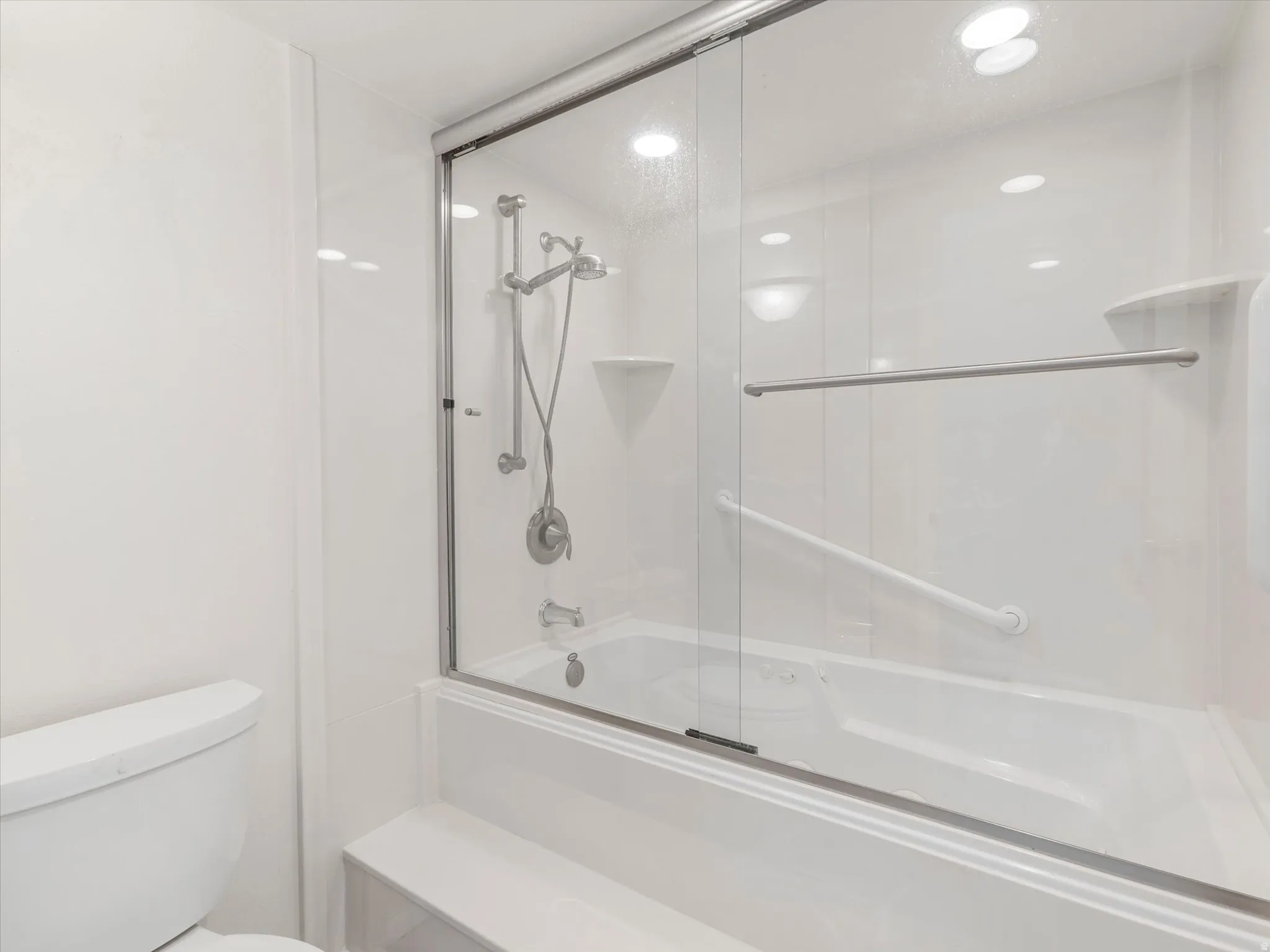 Bathtub with sliding glass enclosure, integrated shower head, grab bars, and recessed lighting