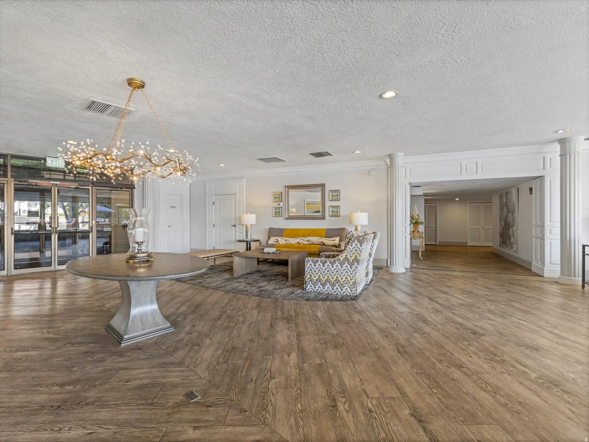 Wood-finish flooring, decorative chandelier, architectural columns, recessed lighting, and a detailed archway