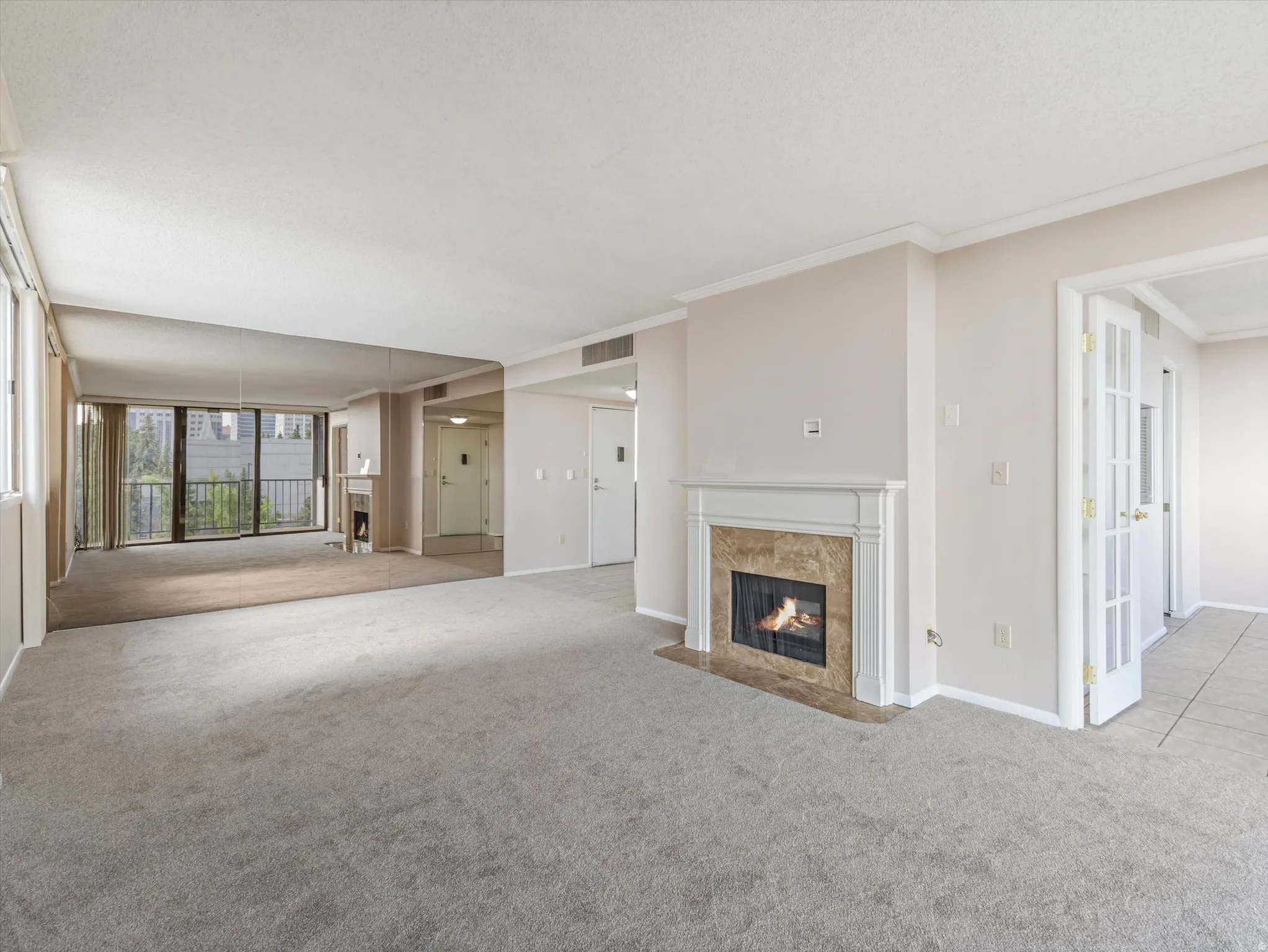 Living area with carpeted flooring, a fireplace featuring a stone surround and white mantel, an expansive mirror wall, and a full-light glass door